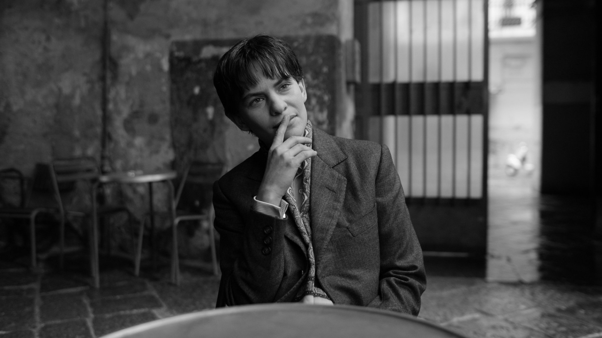 A well-dressed person sits at a cafe table in a laneway.
