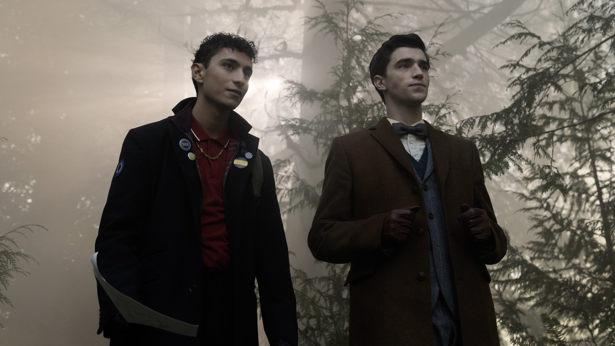 Two young men in long overcoats in the forest.