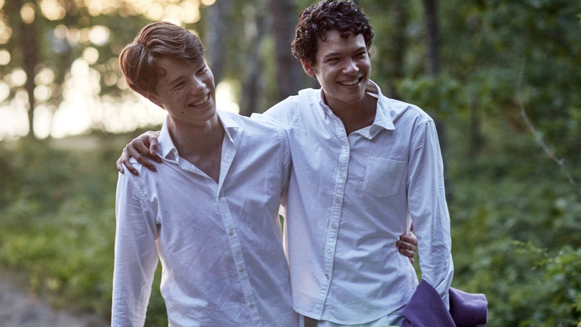 Two young men in white button-up shirts holding each other and smiling.