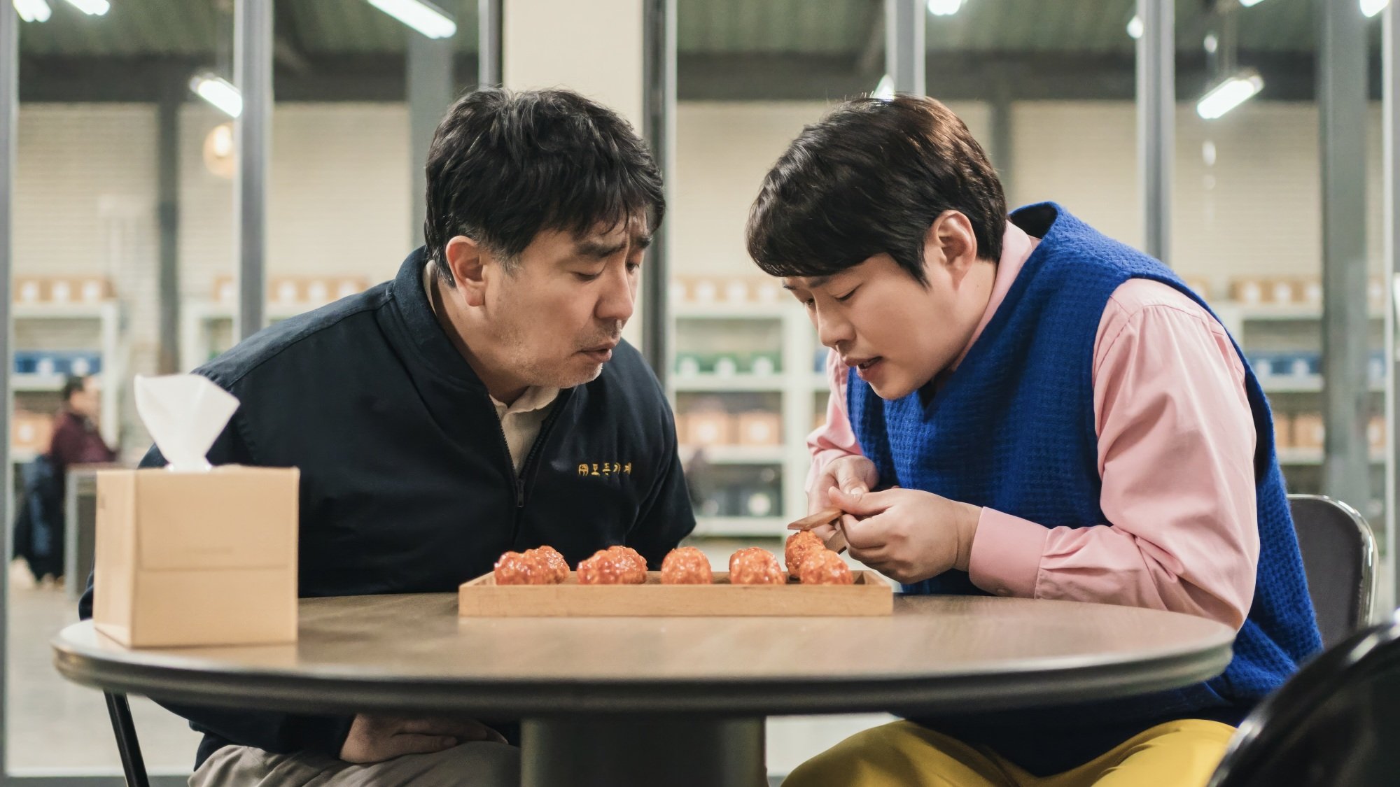 Two men sit at a table, fretting over a box of chicken nuggets.