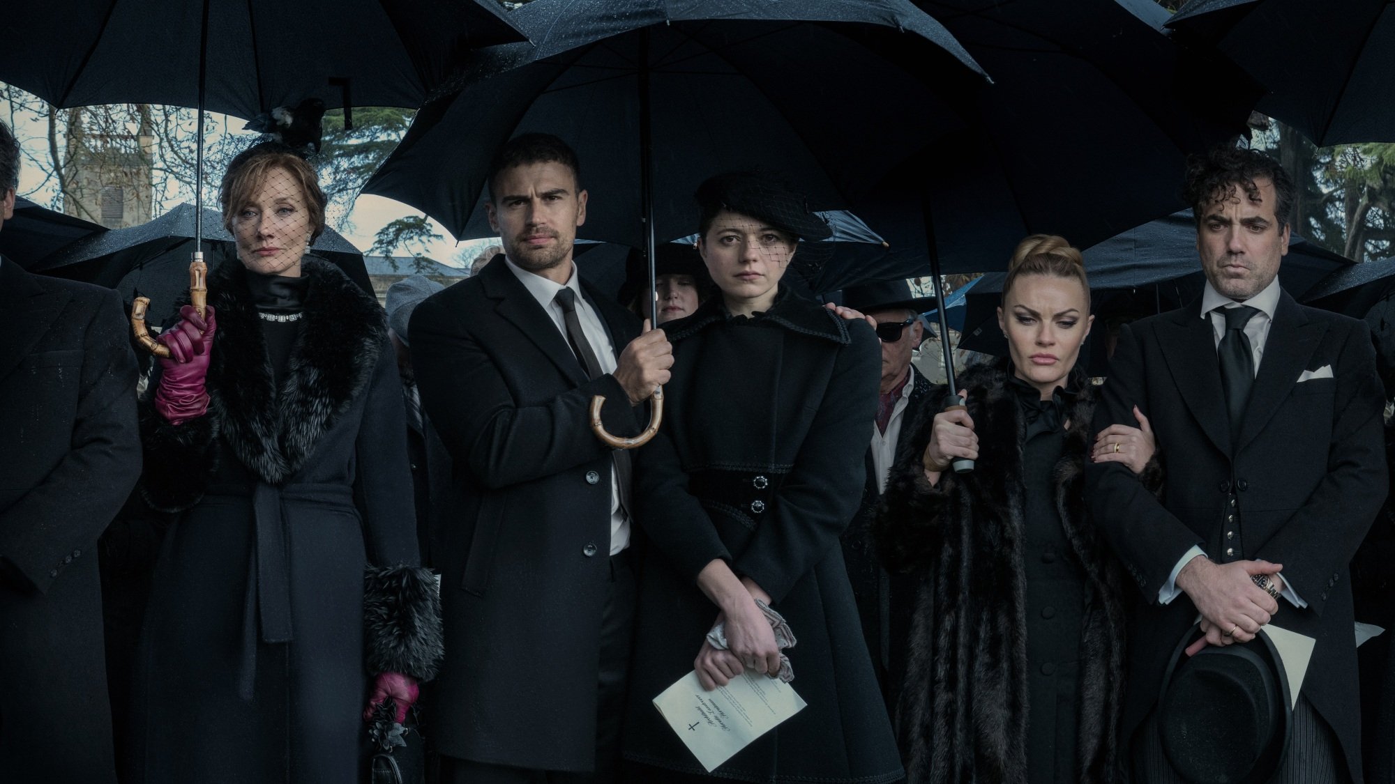 A group of men and women in black funeral attire, holding black umbrellas.