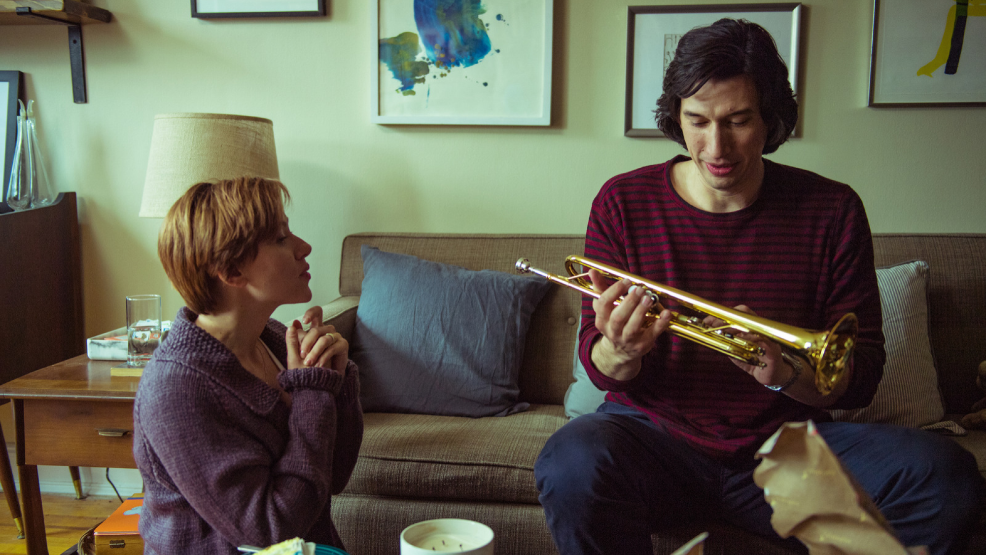 A woman sitting on the floor. A man sitting on the couch holding a trumpet.