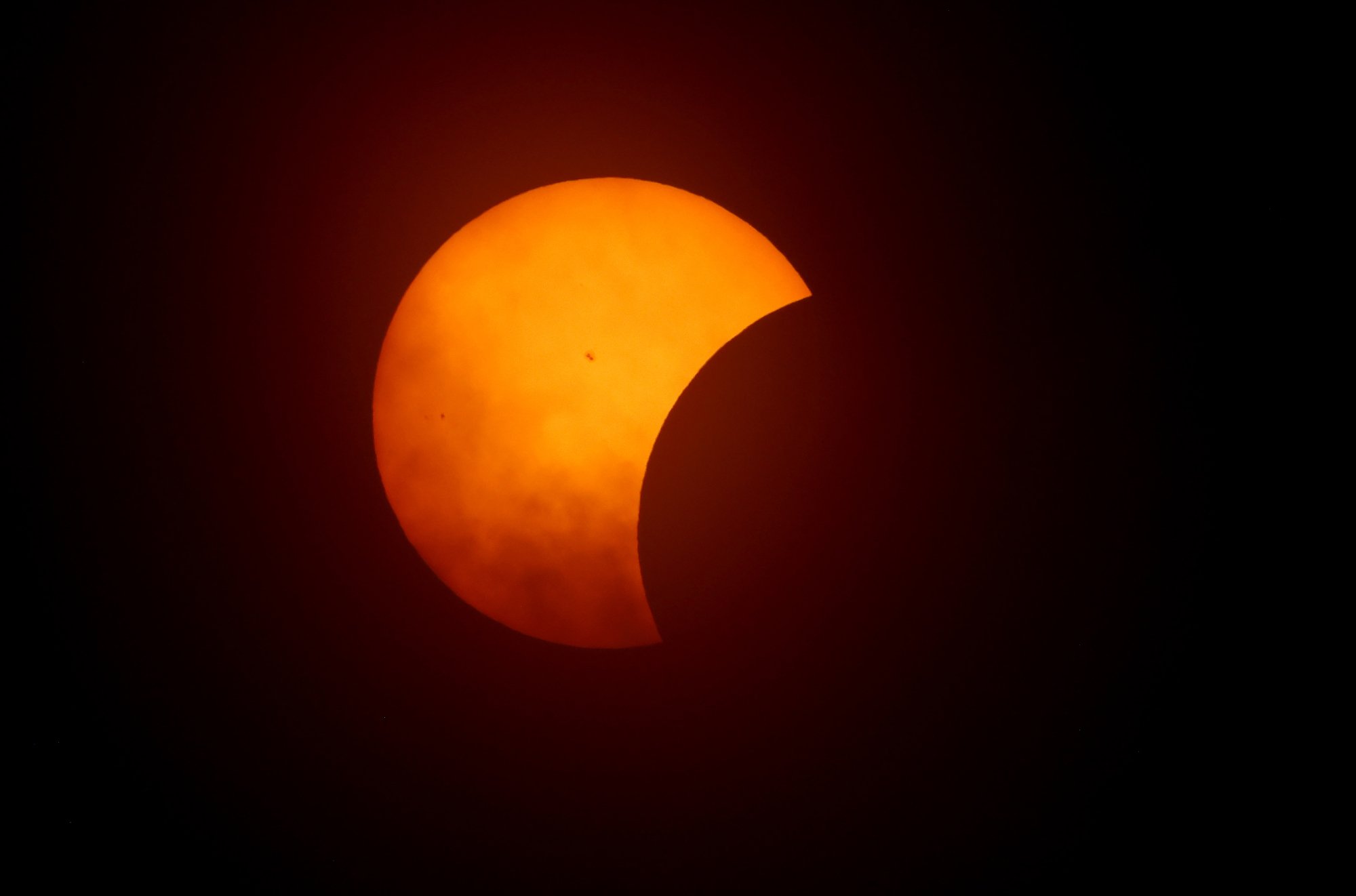 moon creeping over sun, sun is faded orange