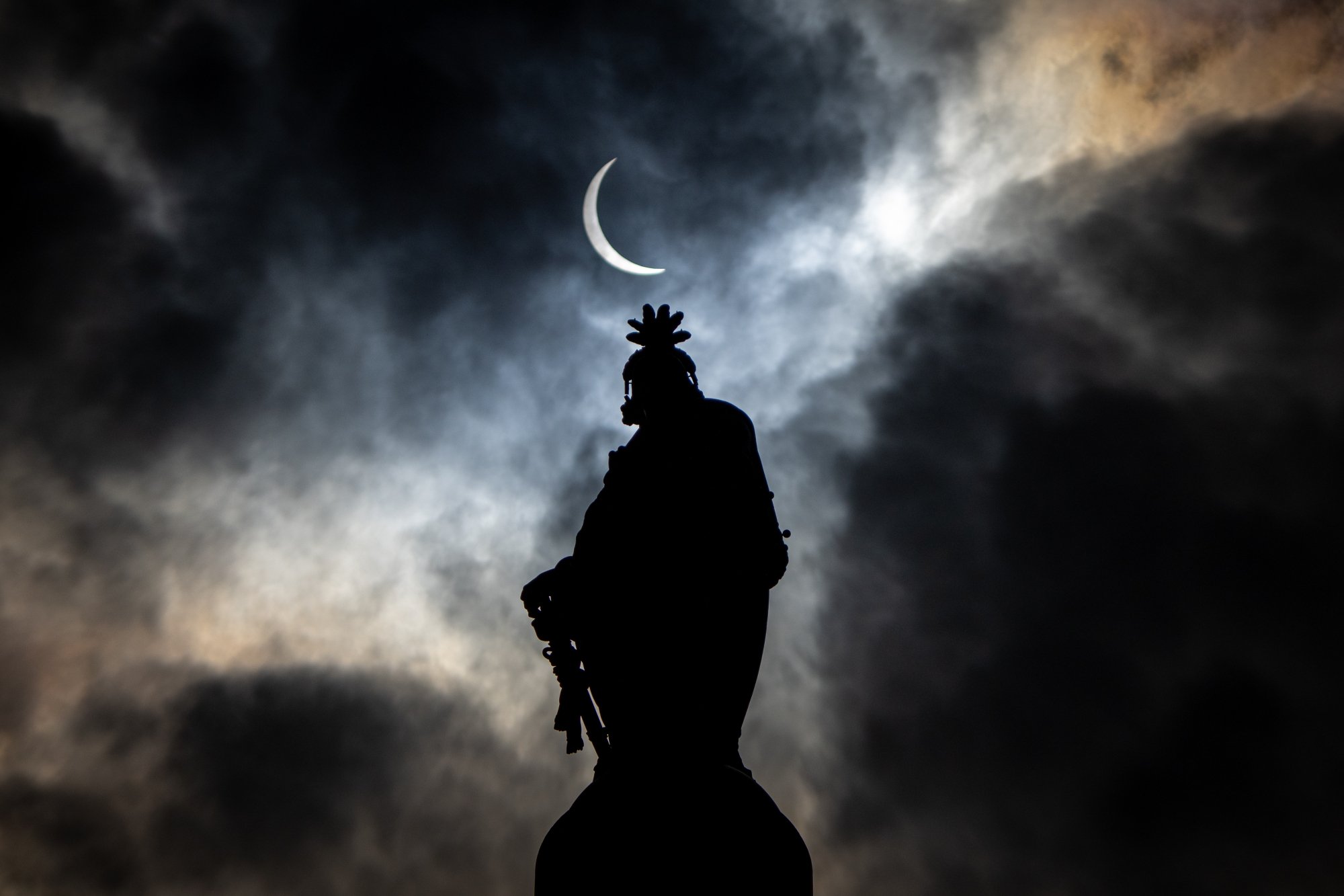 The partial solar eclipse is seen above the Statue of Freedom atop the dome of the U.S. Capitol Building in D.C. the outline of a statue is back lit by a sliver of the sun.