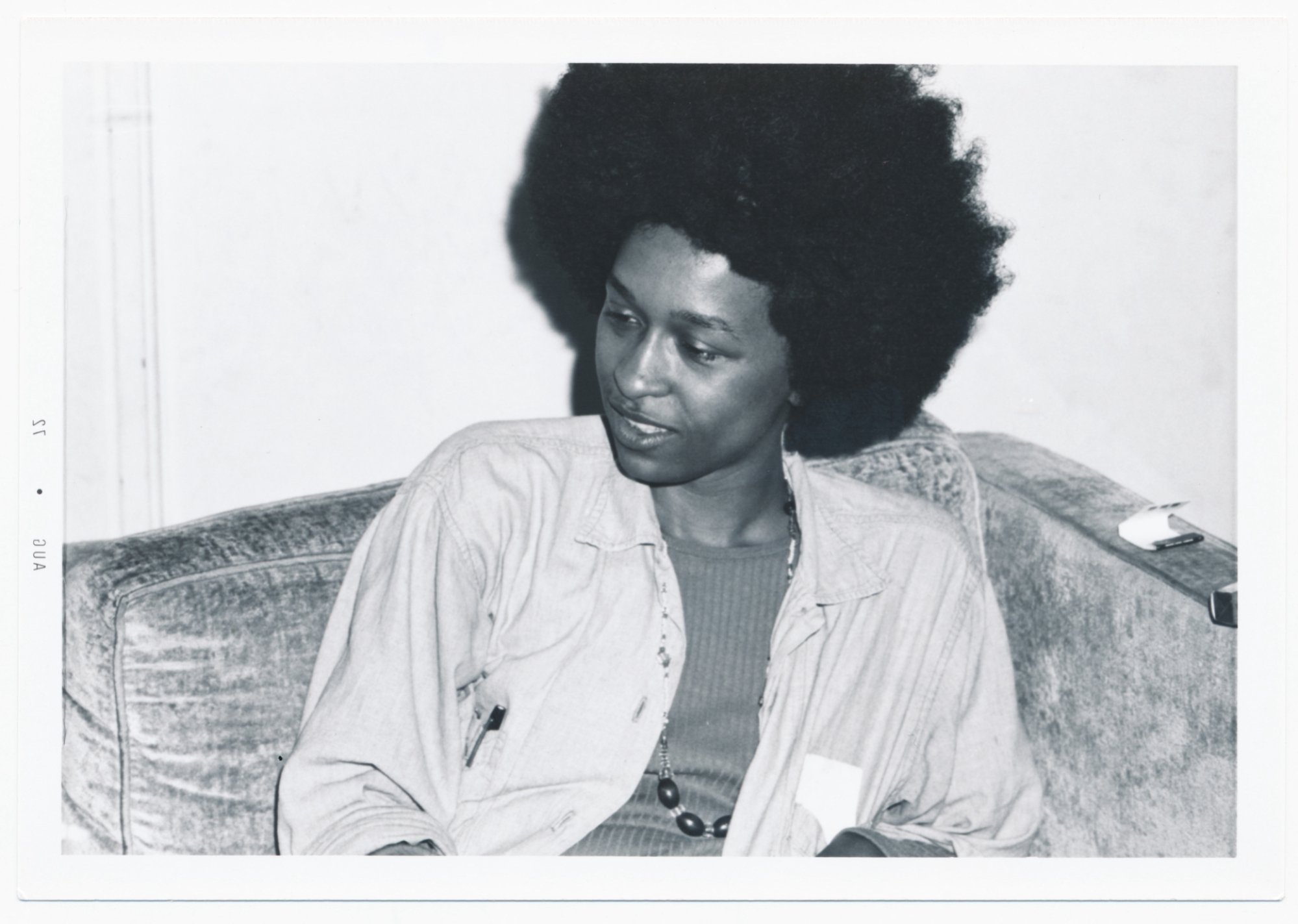 A woman sits on a couch in a black and white photo from the '70s.