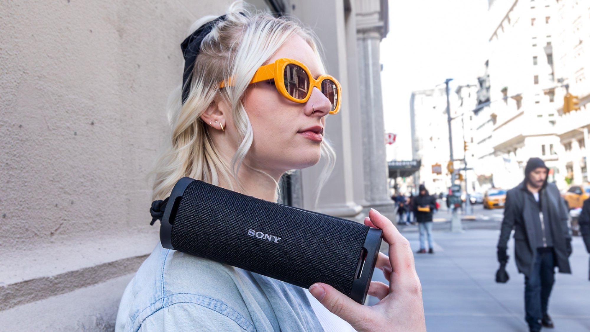 woman wearing sunglasses holding sony speaker on her shoulder outside