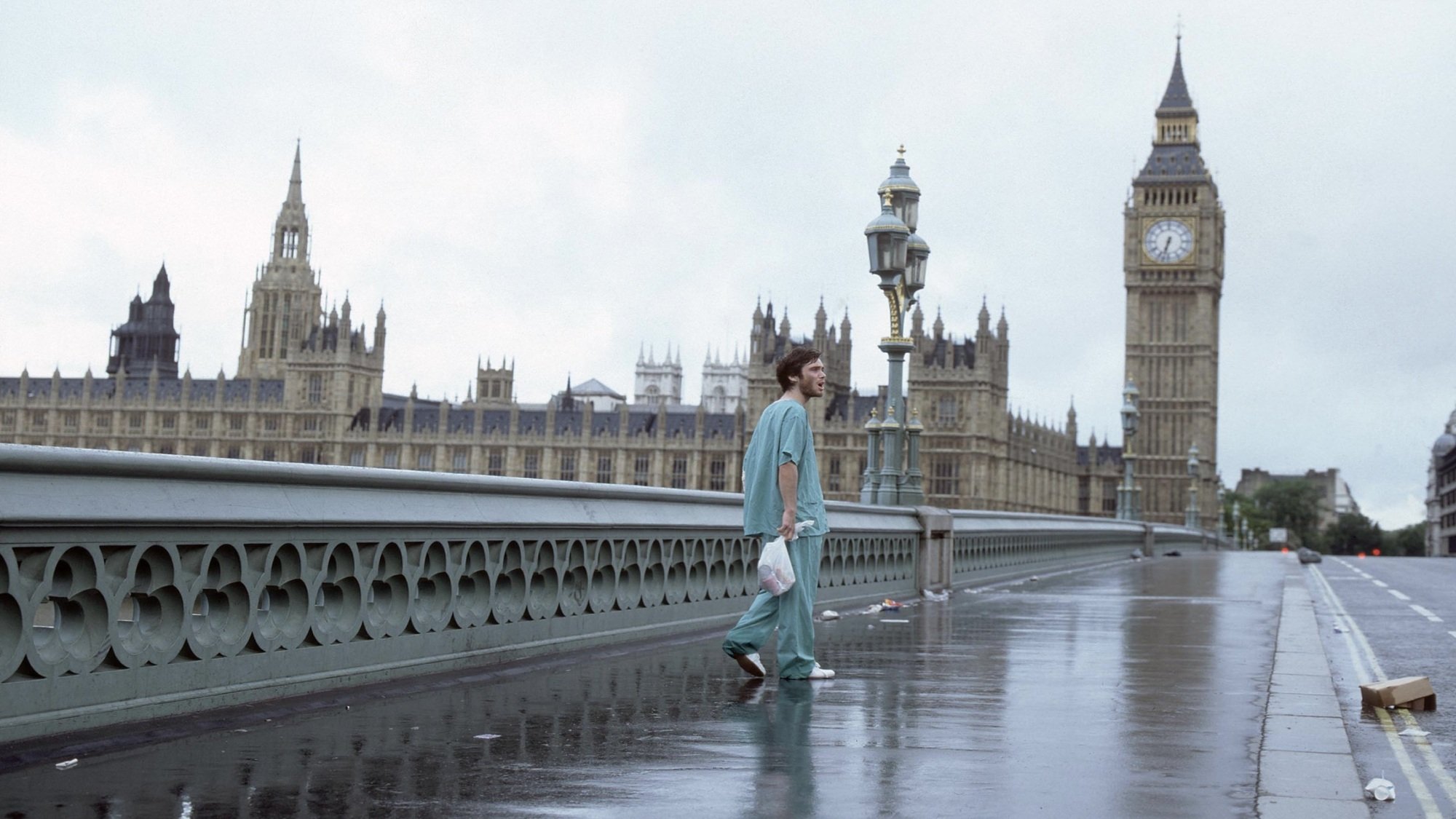 A man in hospital scrubs walks across a deserted Westminster Bridge towards Big Ben.