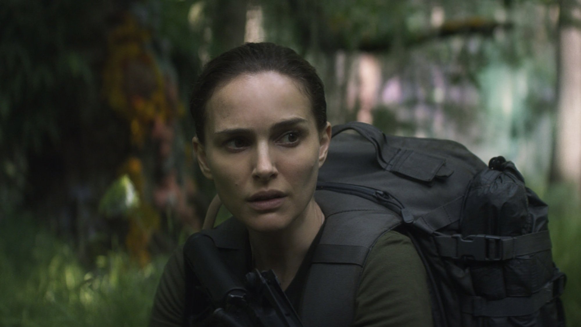 A woman holding a gun walks through a shimmering forest.