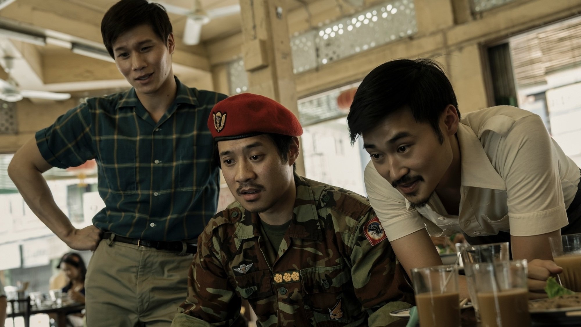 Three men in a cafe look down at a baby, who is off-camera.