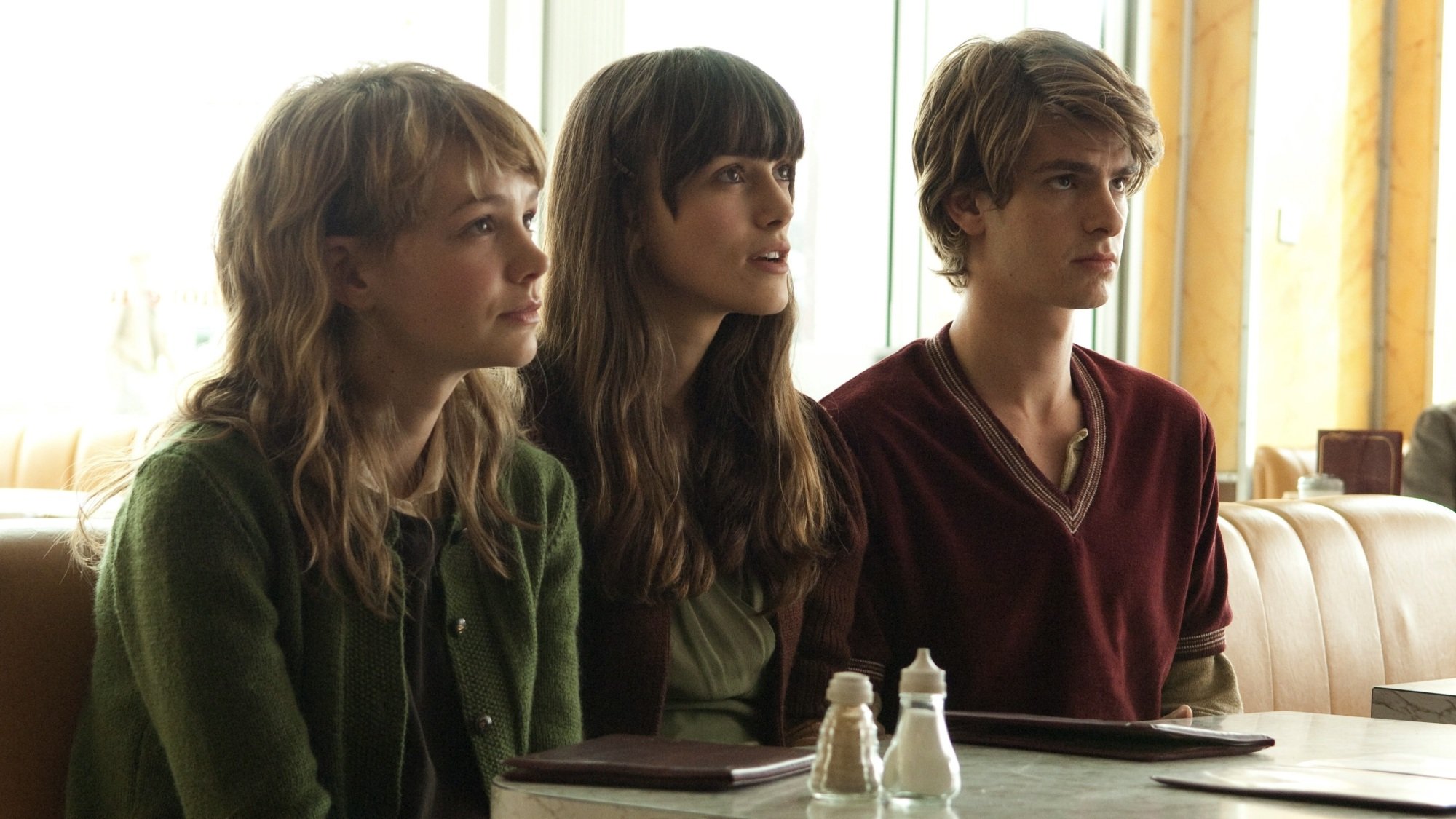 Two young women and a young man sit on the same bench at a diner table.