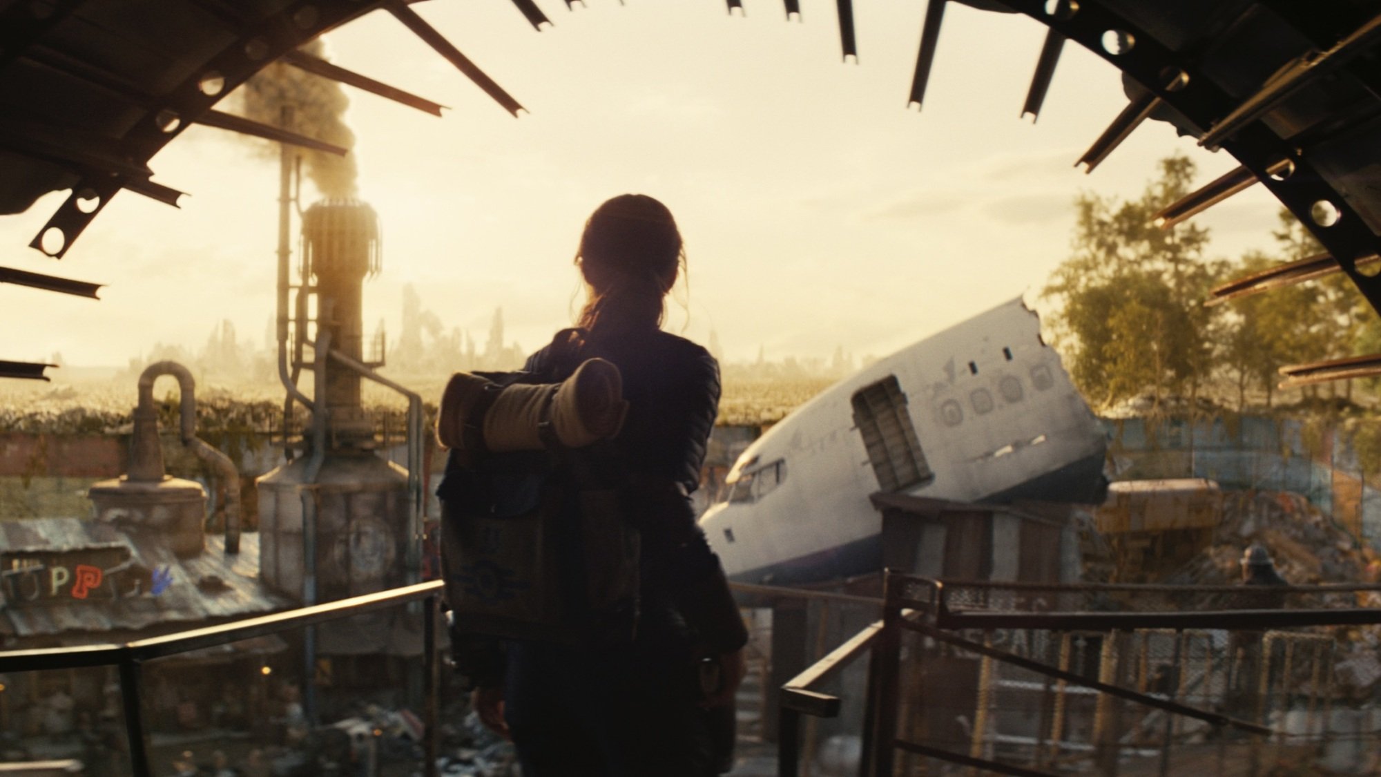 Lucy from "Fallout" walks through a tunnel into a scrapyard.