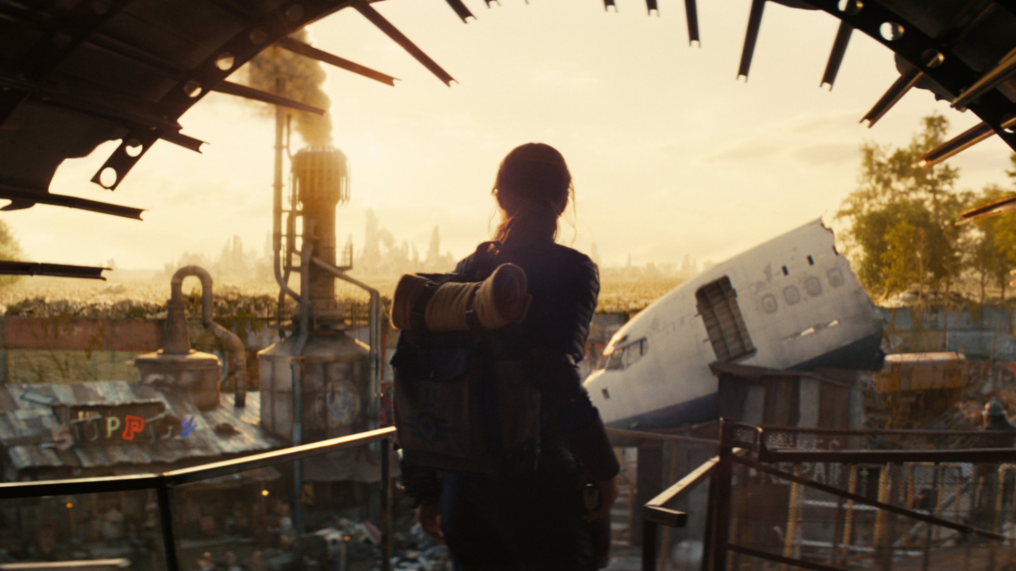 A woman wearing a backpack stands at the edge of a ramshackle town in "Fallout".