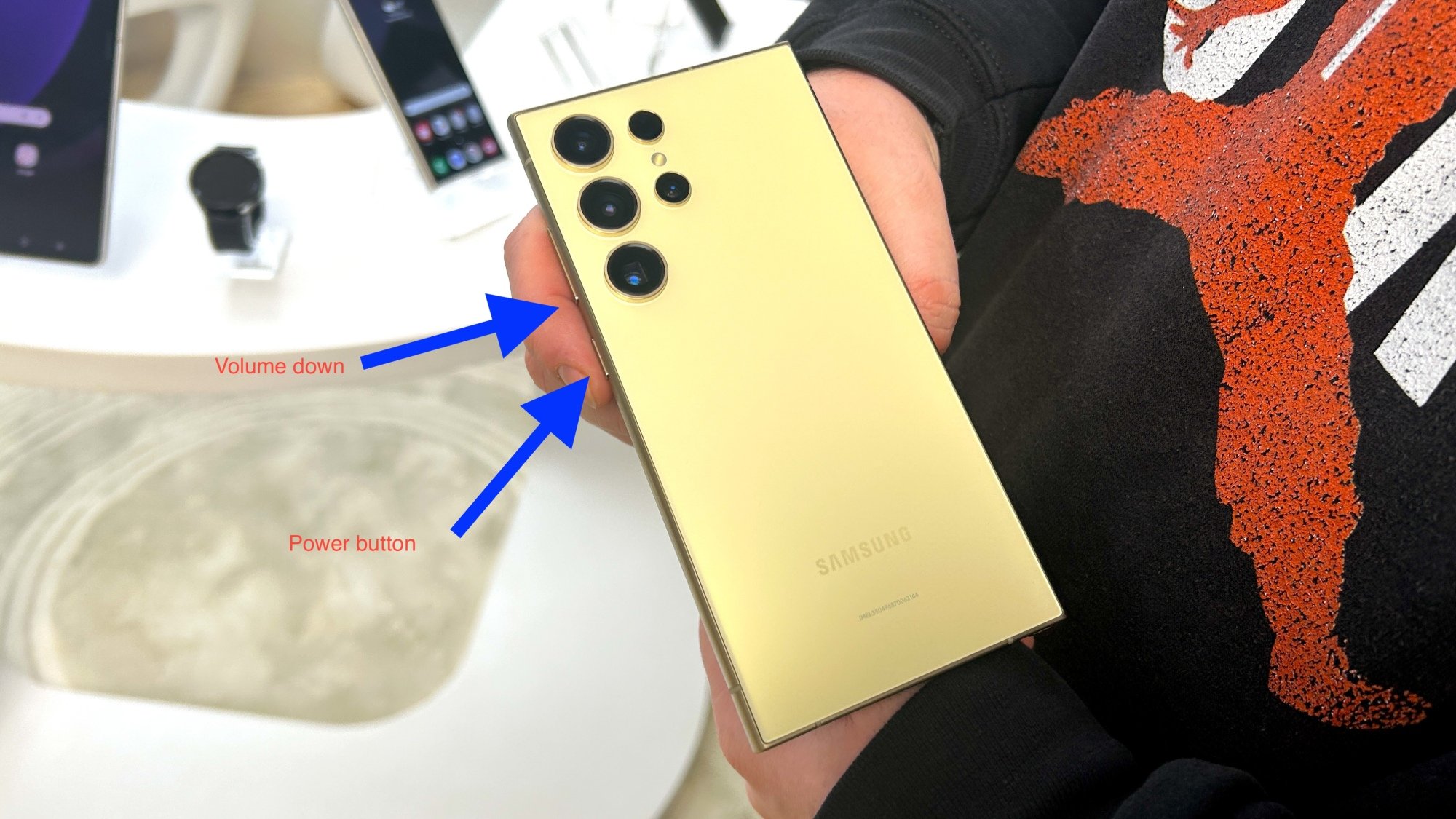 Two blue arrows pointing to power and volume down buttons on Galaxy S24 phone