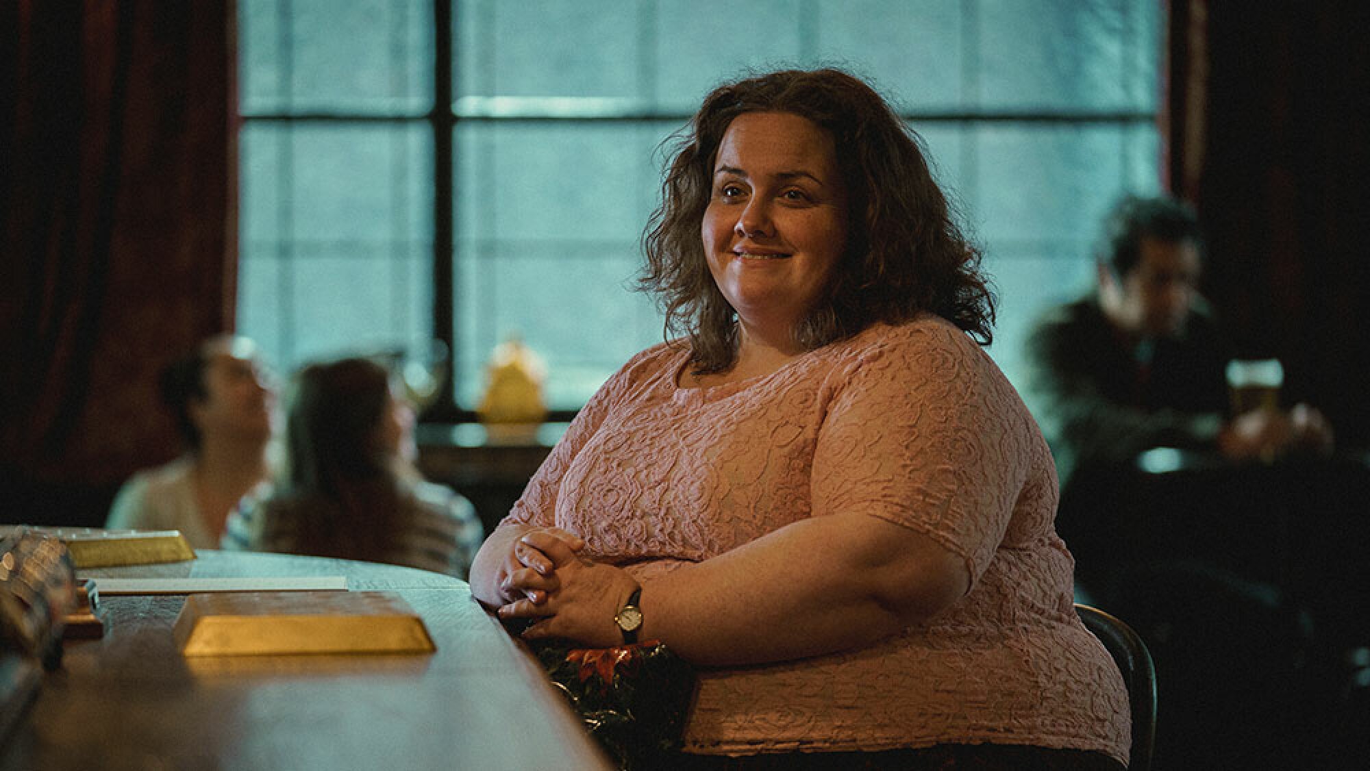 A woman sits on a pub stool in front of the bar.