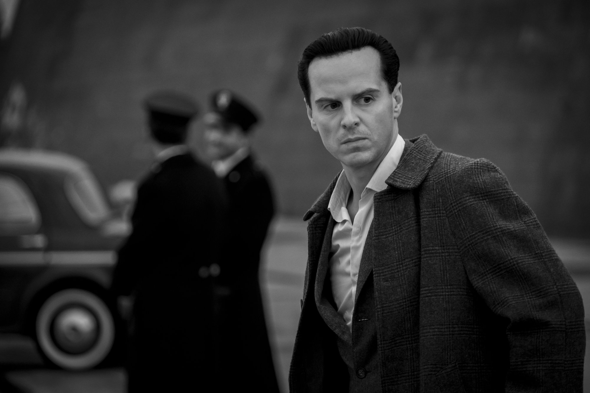 A man in a suit looks off camera, as two police officers stand nearby.